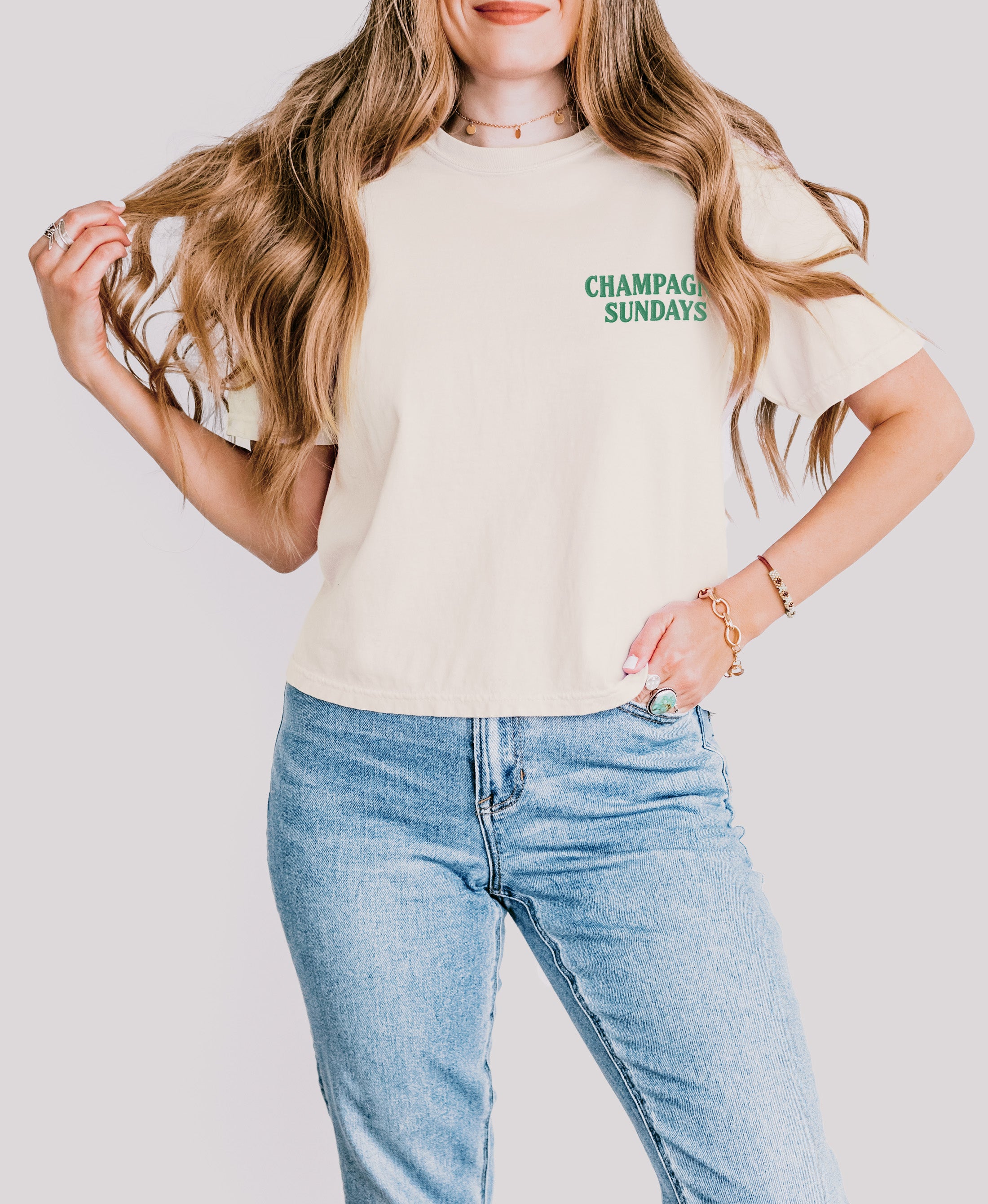 Model wearing green embroidered Champagne Sundays crop tee in cream, left pocked location