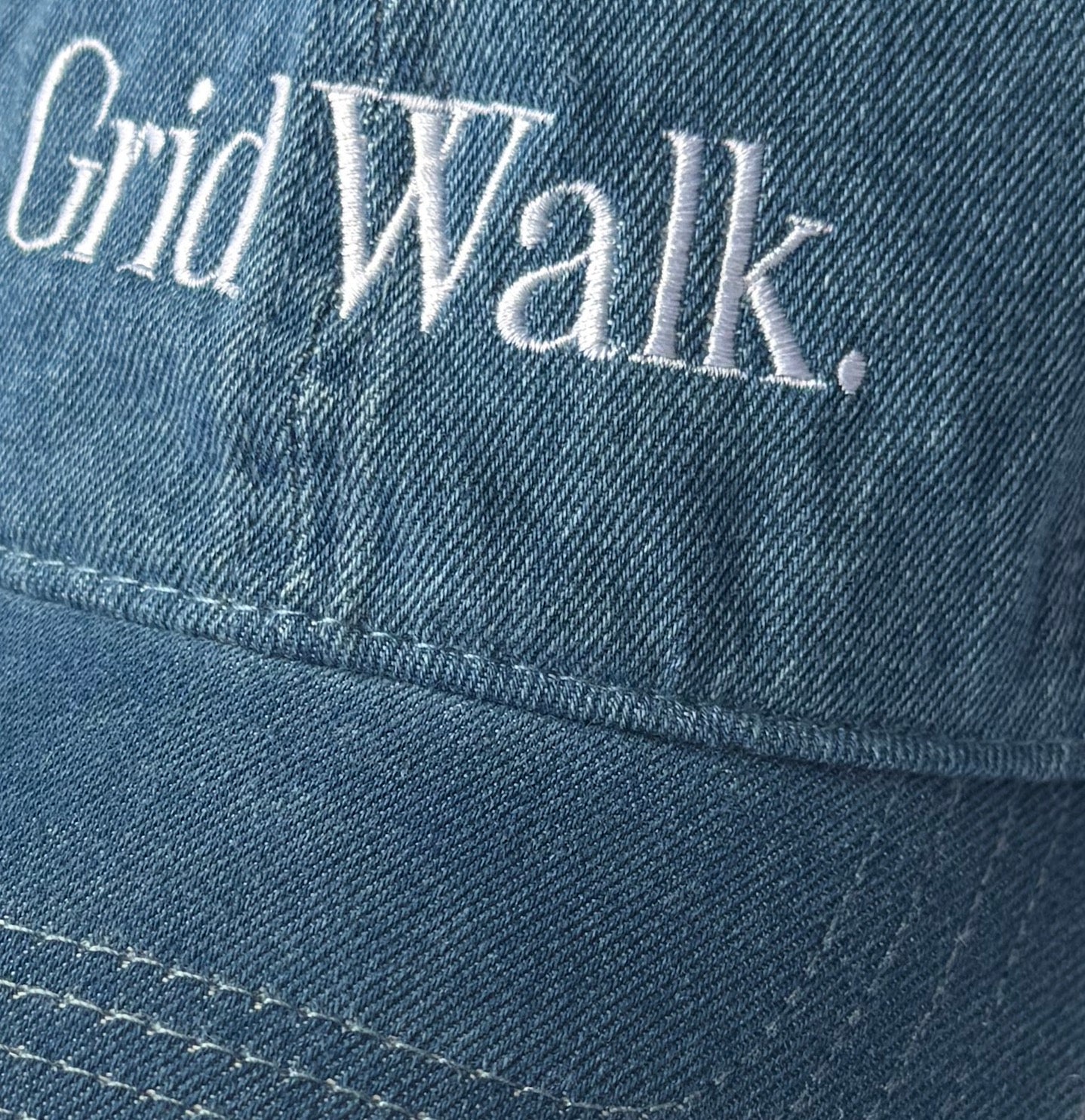 Close-up of Grid Walk white embroidery on denim dad hat