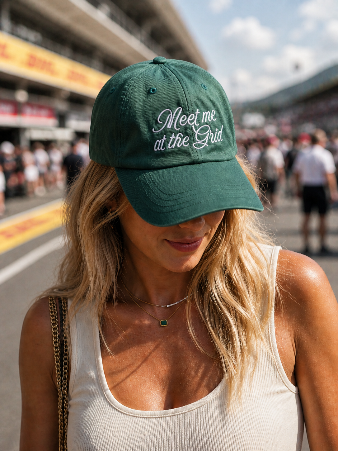 Woman wearing a green cap with 'Meet me at the Grid' text on a race track.
