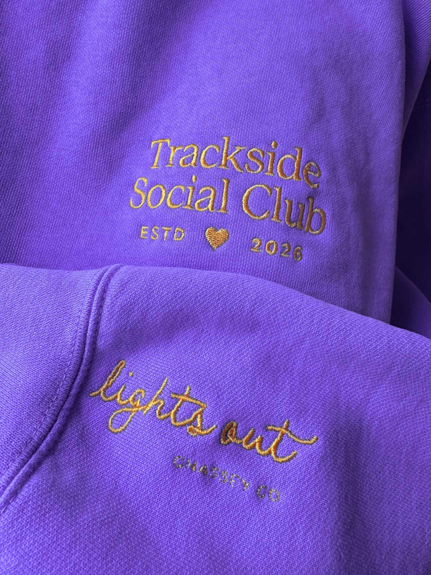 Purple sweatshirt with 'Trackside Social Club' and 'lights out' text in gold.